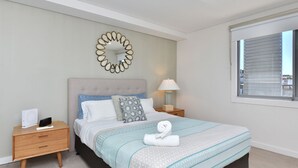 A bedroom with a bed, a bedside table, a lamp, a mirror, and a window.