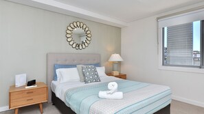 A bedroom with a bed, a bedside table, a lamp, a mirror, and a window.