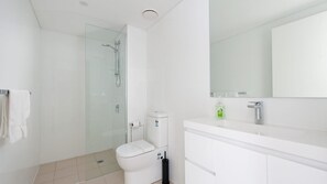 A modern bathroom with a glass shower enclosure, a toilet, a sink with a mirror, and a toilet paper holder.