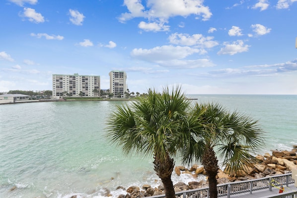 A coastal view with a clear sky, calm sea, and two prominent buildings in the background. - Land's End 302 building 5 Beautiful Updates | Stunning views | Unique Floor Plan (Treasure Island)