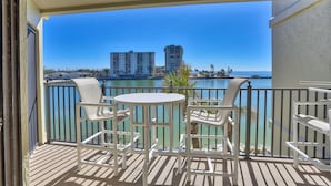A balcony with white chairs and a table, overlooking a body of water and buildings. - Land's End 302 building 5 Beautiful Updates | Stunning views | Unique Floor Plan (Treasure Island)