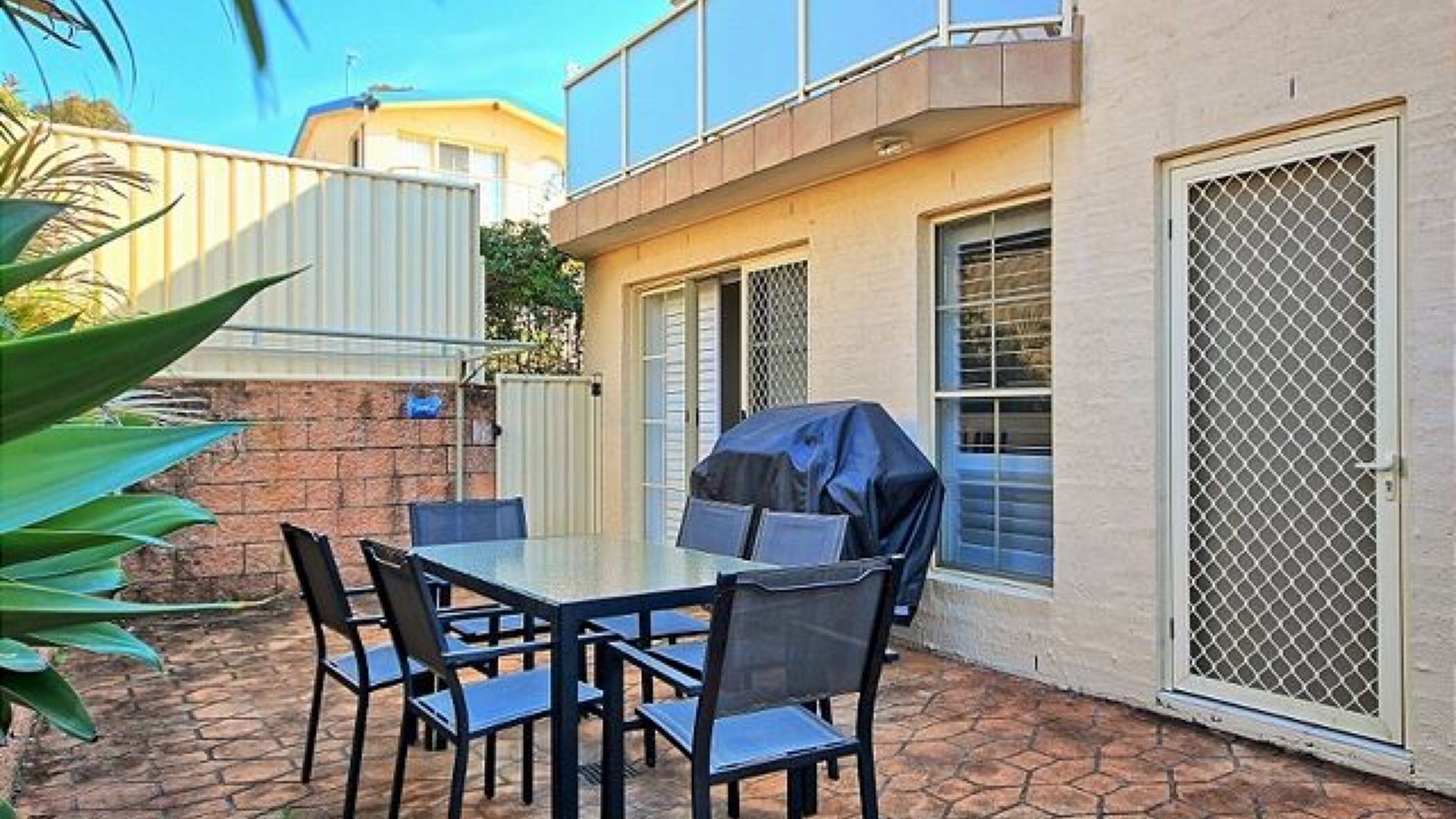 Patio esterno con tavolo e sedie, un barbecue e un cancello di sicurezza.