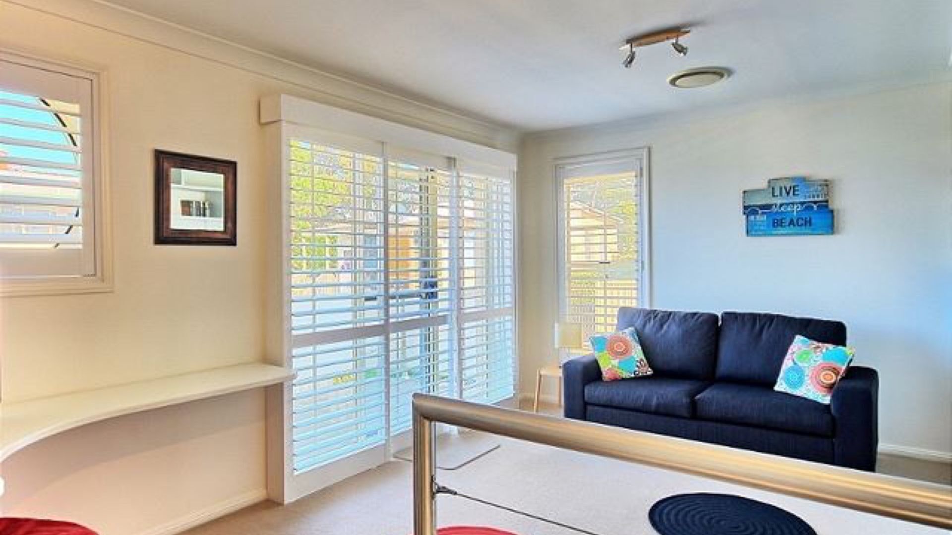 Una habitación con un sofá azul oscuro, un cuadro en la pared y un letrero que dice 'LIVE BEACH'.