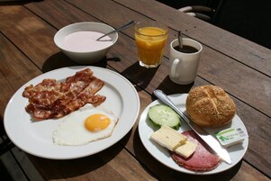 Prato de café da manhã com bacon, ovo, queijo, presunto e um pão.