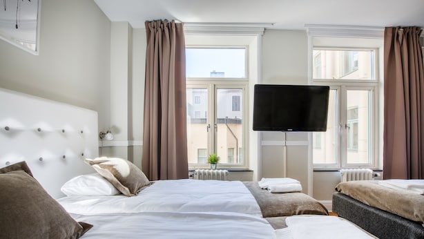 Una habitación de hotel con una cama grande, televisión y ventana con cortinas.