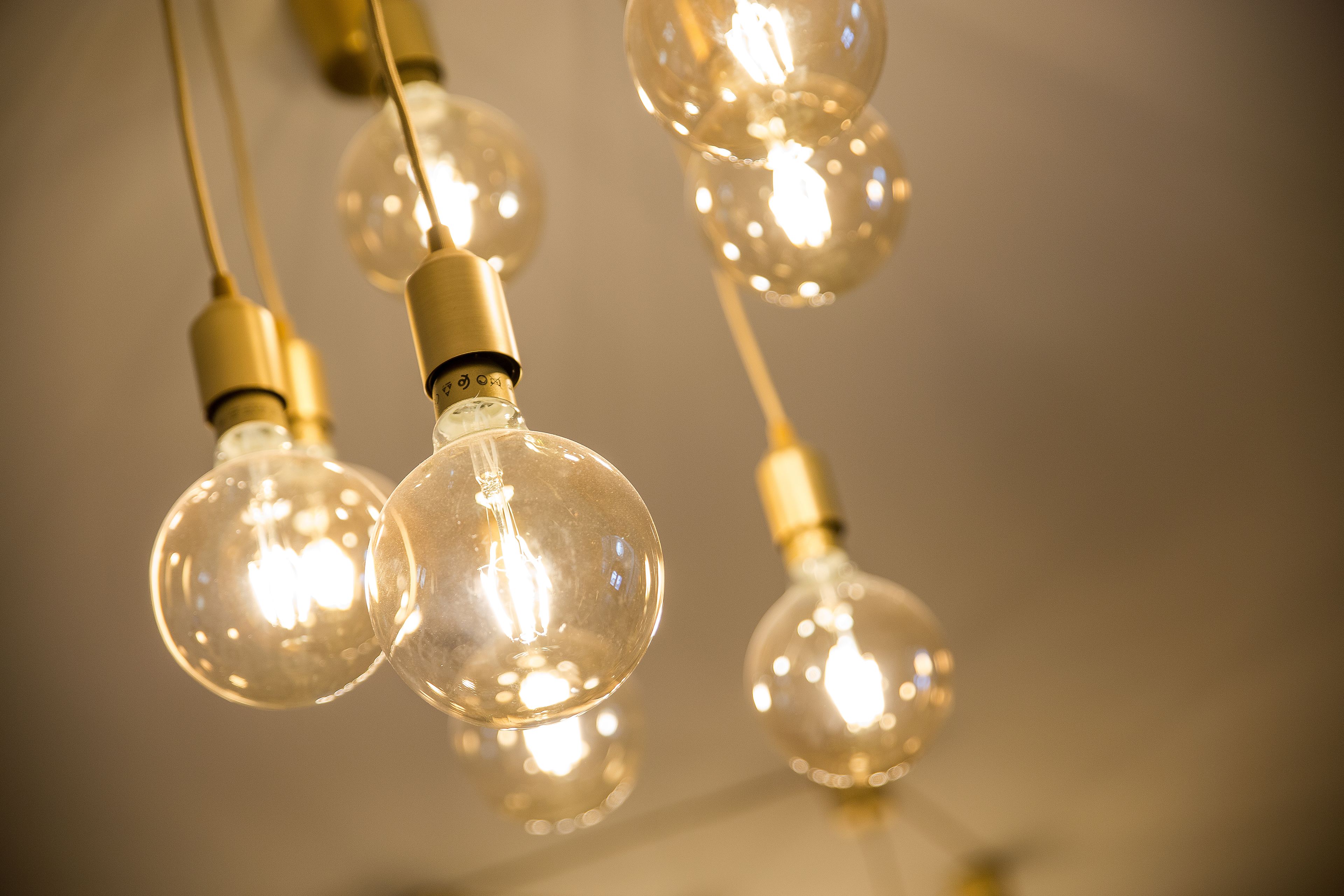 A close-up of several clear glass light bulbs with visible filaments, hanging from a ceiling.