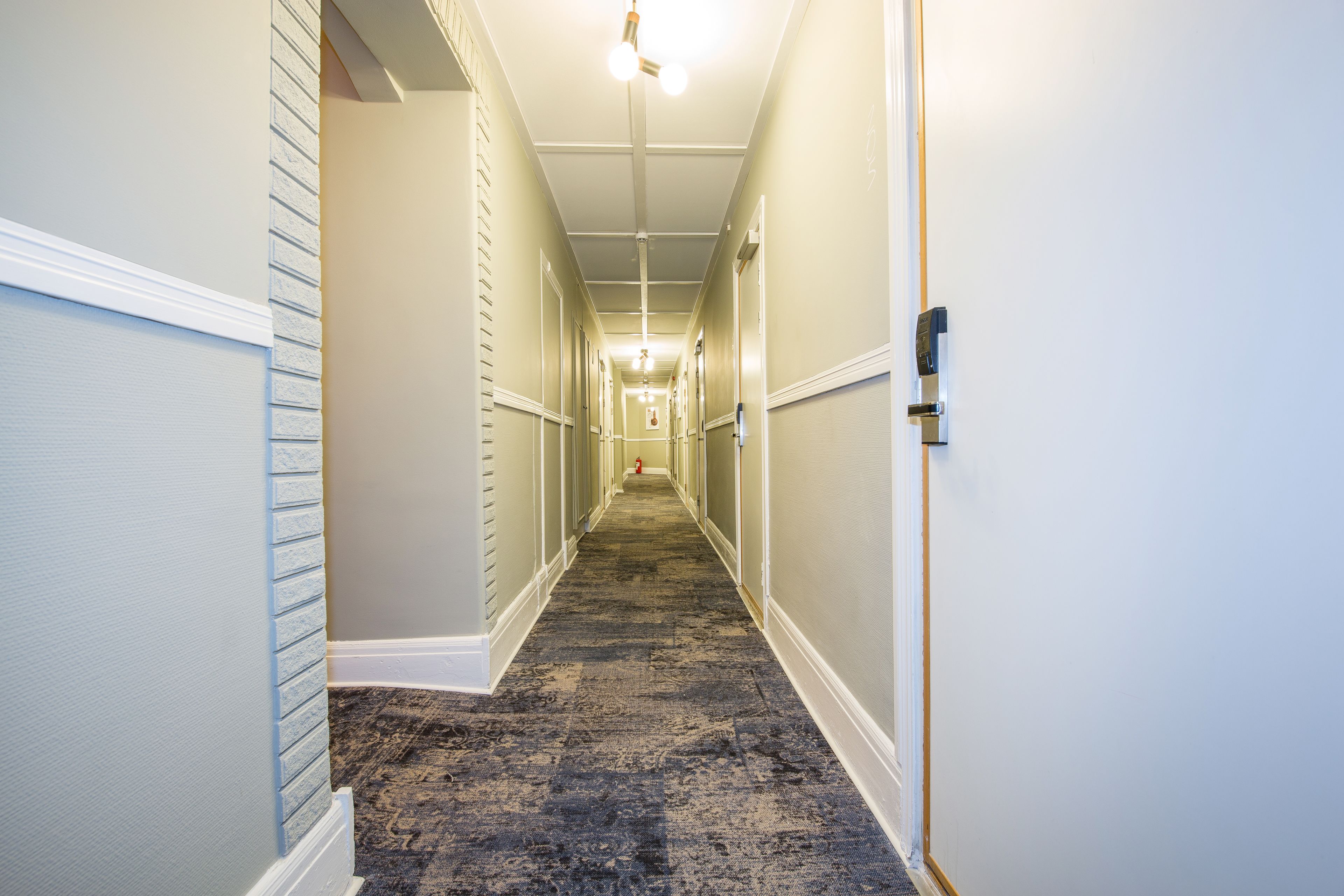 A hotel hallway with a carpeted floor, white walls, and a door on the right.