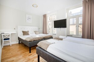 Quarto de hotel com duas camas, uma escrivaninha, uma televisão e uma janela com cortinas.