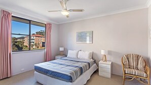 Una camera da letto con un letto, comodini, una sedia, una ventola a soffitto e una finestra con tende.