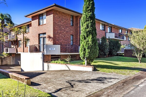 A two-story residential building with a brick facade, a small front garden, and a clear blue sky.