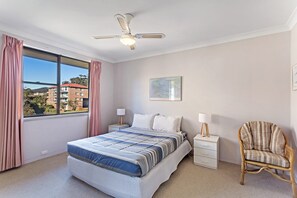 Ein Schlafzimmer mit einem Bett, Nachttischen, einem Sessel, einem Deckenventilator und einem Fenster mit Vorhängen.