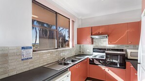 Una cucina con mobili rossi, un fornello, un forno, un microonde e una finestra vista palme.