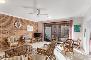 Ein Wohnzimmer mit Backsteinwänden, Korbmöbeln, einem Fernseher und einer Glastür, die zu einem Außenbereich führt.