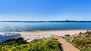 Una platja amb un cel clar, aigua tranquil·la i un camí que condueix a una construcció al costat de la platja.