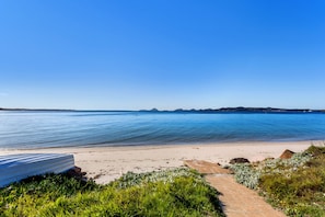 Een strand met een heldere lucht, rustig water en een pad dat leidt naar een gebouw aan het strand.