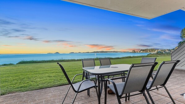 An outdoor patio with a table and chairs, overlooking a body of water and distant land.