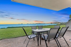 An outdoor patio with a table and chairs overlooking a body of water and distant land. - Harbourside apartment at Soldiers Point (Soldiers Point)