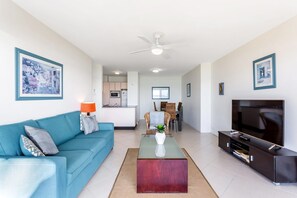 A modern living room with a sofa, coffee table, TV, and artwork on the walls.