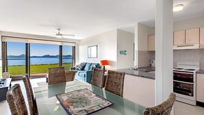 A modern kitchen with a view of the sea, a dining area with wicker chairs, and a large window. - Harbourside, Unit 2/7 Soldiers Point Road - Absolute waterfront unit at Sunrise Beach (Soldiers Point)