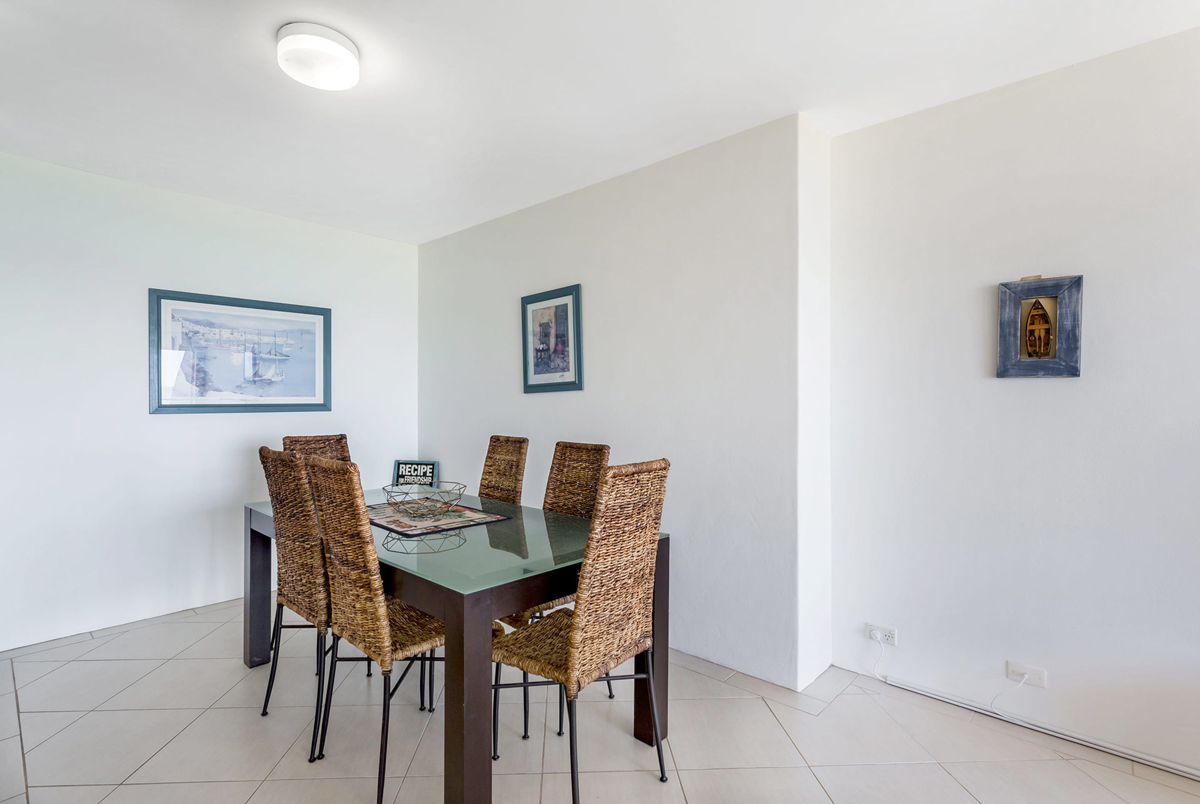 Un coin repas comprenant une table à plateau en verre, six chaises en osier et deux œuvres d’art encadrées accrochées aux murs.