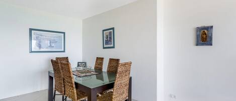 Un comedor con una mesa de vidrio, seis sillas de mimbre y dos cuadros en las paredes.