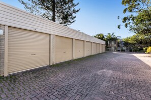 A row of closed storage units with numbered doors, a paved driveway, and trees in the background.