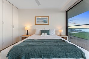 A hotel room with a large bed, two bedside lamps, a framed picture on the wall, and a view of the sea through a large window. - Harbourside apartment at Soldiers Point (Soldiers Point)