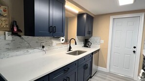 A modern kitchen with dark cabinets, a white countertop, a stainless steel sink, and a coffee maker. - water front,pool,hot tub,fishing,close to beaches (new port richey)