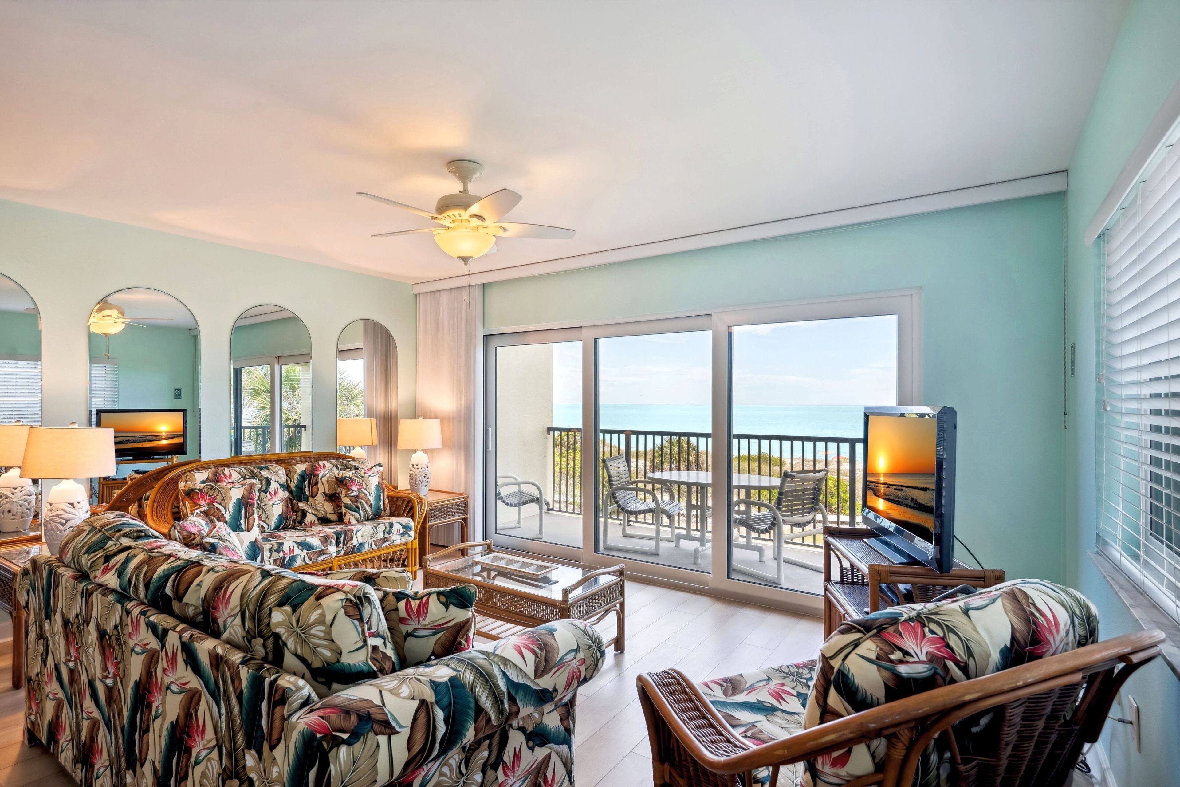 A spacious living area with a sofa, chairs, and a television on a balcony overlooking the sea.