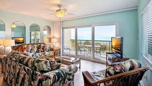A spacious living area with a sofa, chairs, and a television on a balcony overlooking the sea.