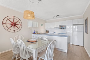 Een moderne keuken met witte kasten, een centraal eiland en een eethoek met een glazen tafel en witte stoelen.