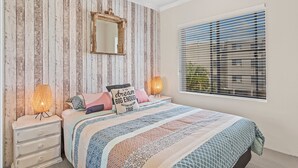 Quarto com cama, penteadeira, espelho, ventilador de teto e janela com persianas.