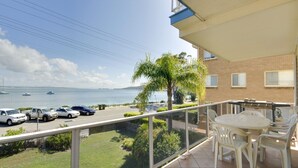 Een balkon met uitzicht op zee, een tafel met stoelen en geparkeerde auto's.