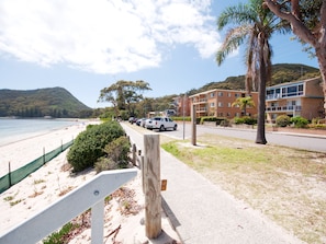A beachfront property with a paved walkway, parked vehicles, and a building with balconies. - Castaways 4 Shoal Bay Apartment with Water Views (Shoal Bay)