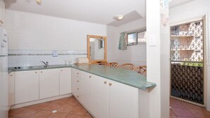 Een compacte keuken met witte kastjes, een groen aanrecht en een raam met uitzicht op buiten.