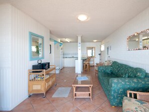 A room with a green patterned sofa, a wooden chair, a small table, and a mirror on the wall. - Castaways 4 Shoal Bay Apartment with Water Views (Shoal Bay)