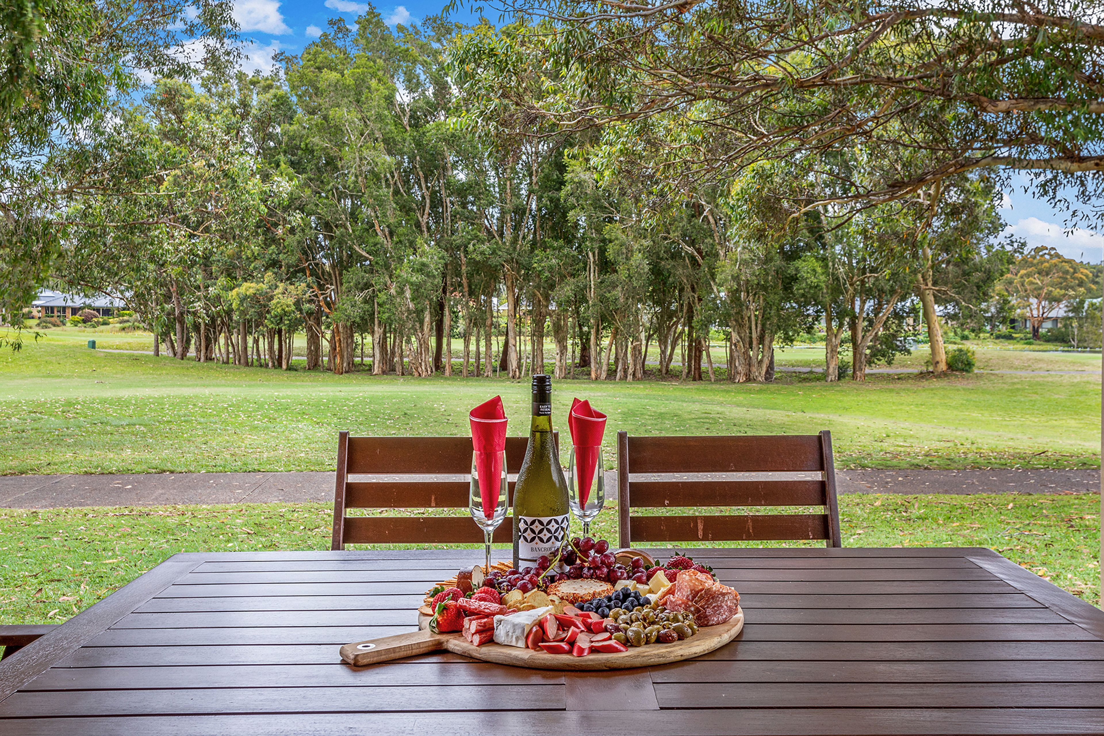 An outdoor dining area with a wooden table set for a meal, surrounded by trees.