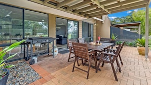Een terras buiten, met een barbecue, eettafel en stoelen.