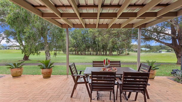 Een terras buiten met een eettafel, omringd door stoelen, onder een houten pergola.