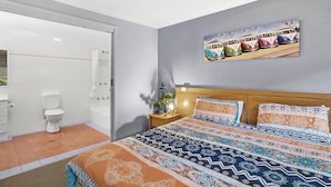 Een slaapkamer met een bed, een nachtkastje, een wanddecoratie en een badkamer met toilet en douche.