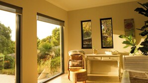 A modern living room with a large sliding glass door leading to a pool, a comfortable seating area with a chair and ottoman, a small table with a plant, and a large window with a view of trees. - “ROCKPOOL” Holiday Beach House Margaret River (5 bedrooms,  walk to beach) (Gnarabup)