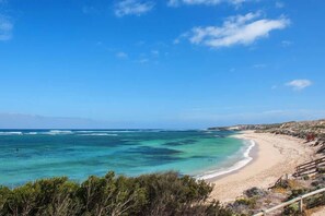 Ein Küstenstrand mit klarem türkisblauem Wasser, Sandufer und Felsen.