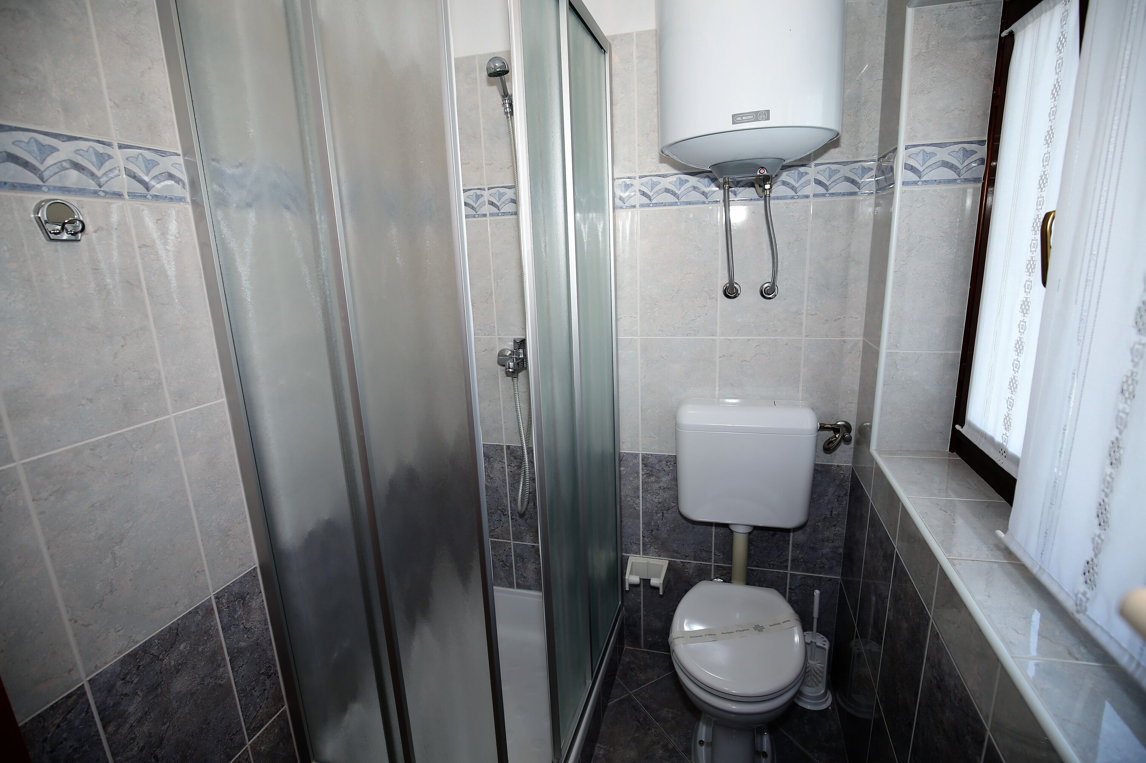 Ein Badezimmer mit Duschkabine, Toilette und Durchlauferhitzer.