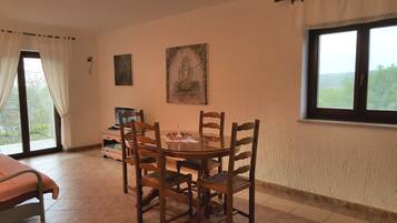 Un comedor con una mesa redonda de vidrio, sillas de madera, un televisor y obras de arte en las paredes.