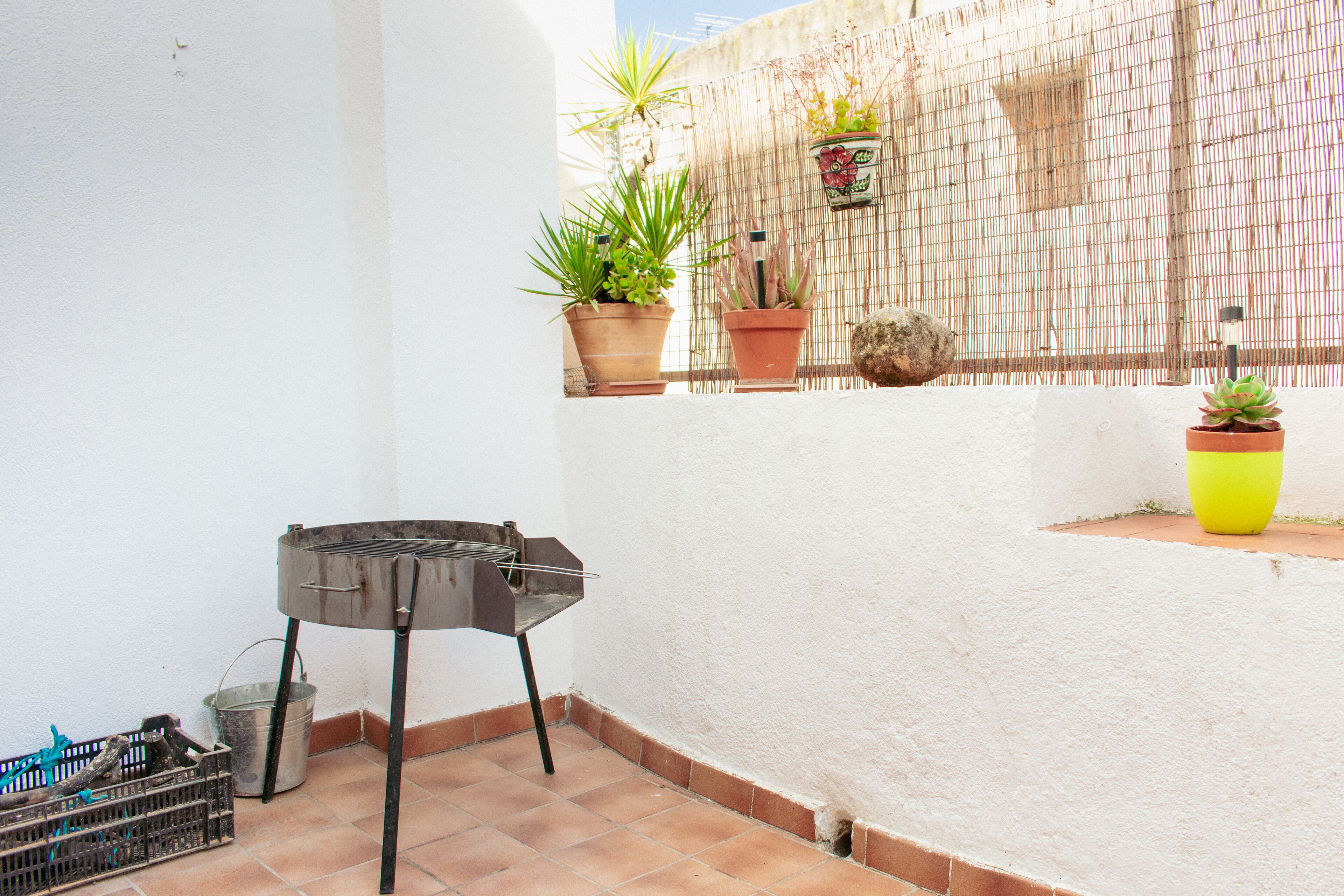 A small outdoor area with a grill, potted plants, and a tiled floor.