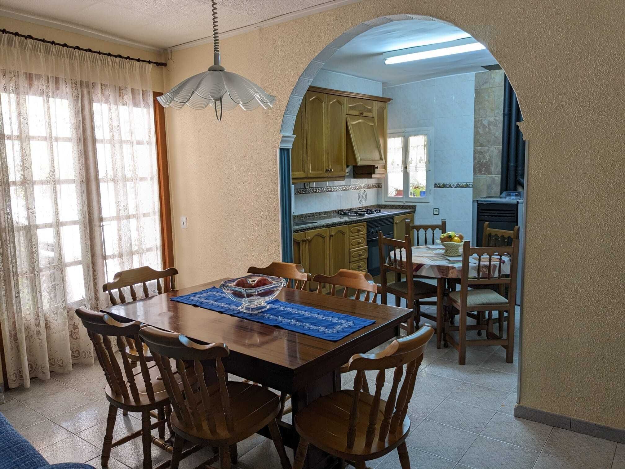 Un comedor con una mesa y sillas de madera, un mantel individual azul y un cuenco de fruta.