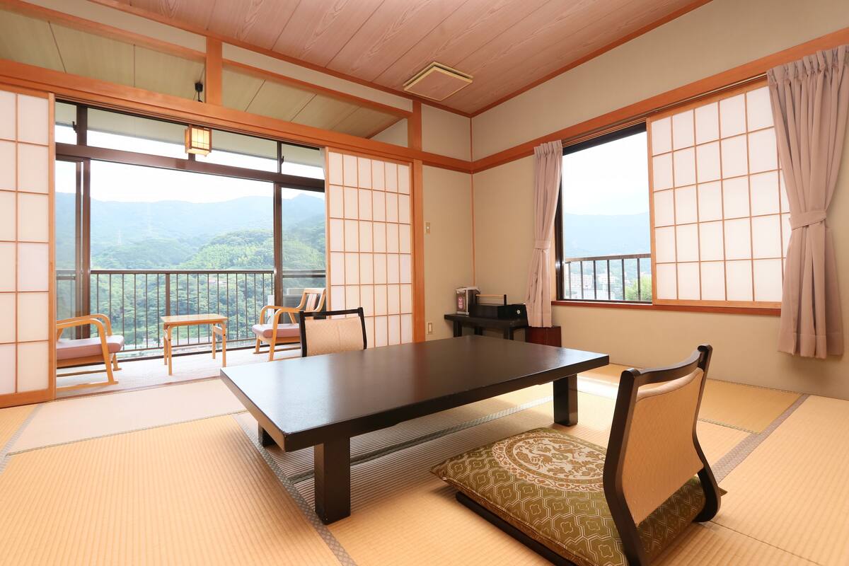 Um quarto japonês tradicional com piso de tatame, uma mesa baixa, cadeiras e portas deslizantes.