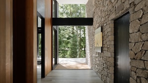 Un interior moderno con pared de piedra, piso de madera y un amplio ventanal con vistas a árboles.