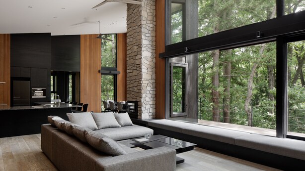 Un interior moderno con una pared de acento de piedra, un ventanal con vistas a un bosque y una cocina minimalista.