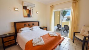 A hotel room with a bed, a nightstand, an air conditioning unit, a chair, and a view of the outside. - Casa Mira Luz, villa with private pool (Praia da Luz)